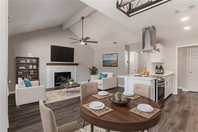 dining area with ceiling fan, dark hardwood / wood-style floors, lofted ceiling with beams, and a tile fireplace