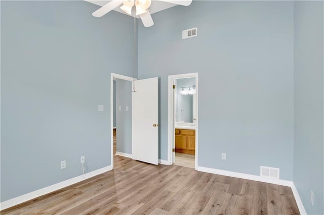 unfurnished bedroom featuring light wood-style floors, a towering ceiling, baseboards, and visible vents
