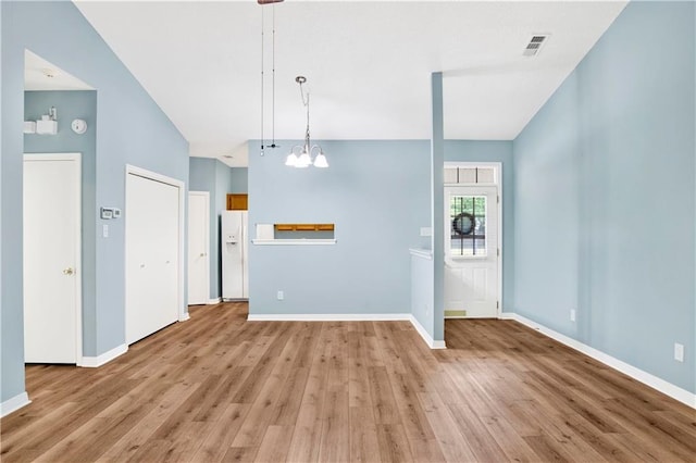 unfurnished living room with baseboards, visible vents, an inviting chandelier, and light wood-type flooring