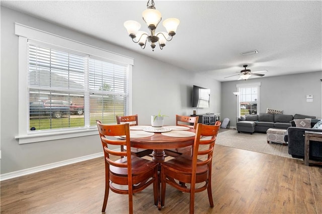 dining space featuring ceiling fan with notable chandelier, a textured ceiling, baseboards, and wood finished floors