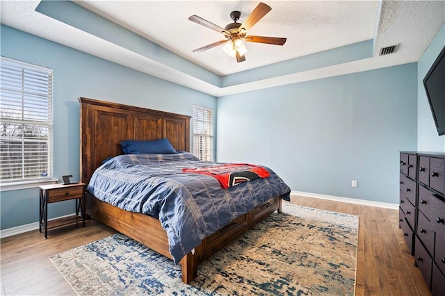 bedroom with visible vents, a raised ceiling, and wood finished floors