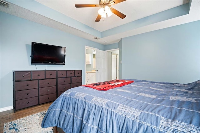 bedroom with a tray ceiling, visible vents, baseboards, and wood finished floors