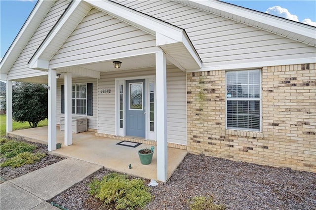 view of exterior entry featuring covered porch and brick siding