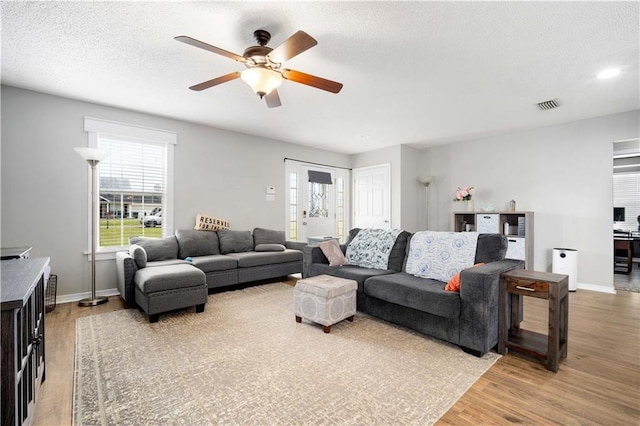 living room featuring baseboards, visible vents, a ceiling fan, a textured ceiling, and light wood-type flooring