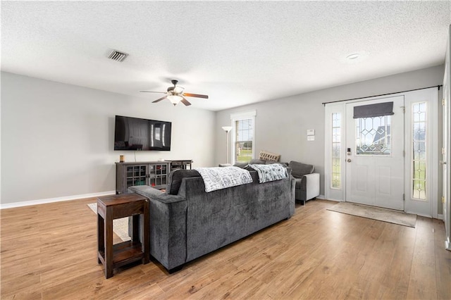 living room with visible vents, baseboards, a ceiling fan, light wood-style flooring, and a textured ceiling