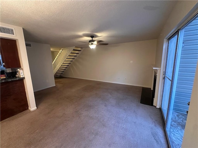 unfurnished living room featuring ceiling fan, a textured ceiling, and dark carpet