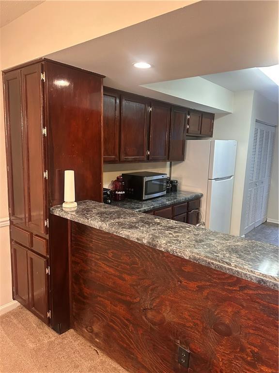 kitchen featuring light carpet, white refrigerator, and dark stone countertops