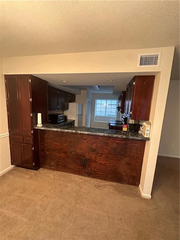 kitchen with dark brown cabinetry, a textured ceiling, white fridge, and light carpet