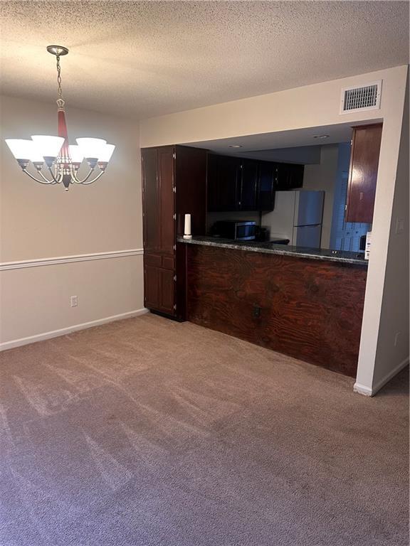 kitchen with hanging light fixtures, white refrigerator, carpet flooring, a textured ceiling, and an inviting chandelier