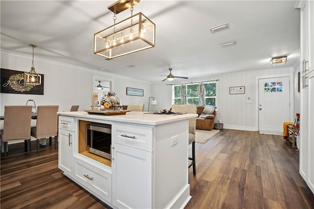 kitchen featuring dark hardwood / wood-style flooring, a center island, hanging light fixtures, ceiling fan, and white cabinets