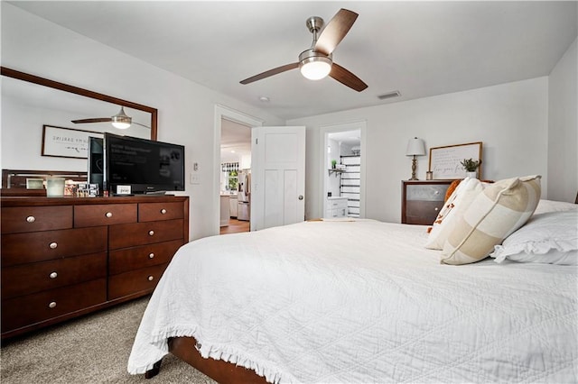 carpeted bedroom with a spacious closet, ceiling fan, and ensuite bath