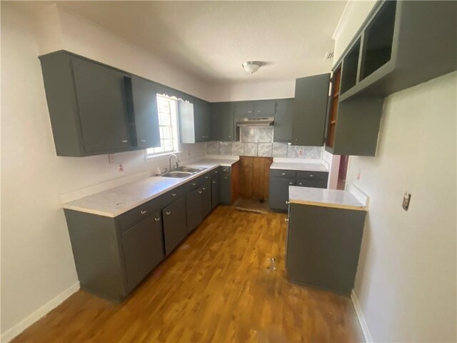 kitchen with light countertops, baseboards, wood finished floors, under cabinet range hood, and a sink