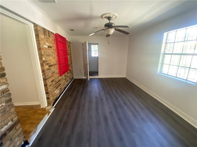 spare room with baseboards, wood finished floors, ceiling fan, and brick wall