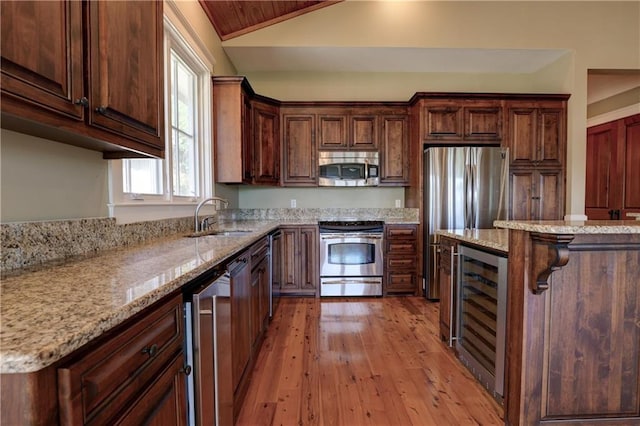 kitchen featuring beverage cooler, light hardwood / wood-style flooring, vaulted ceiling, sink, and appliances with stainless steel finishes