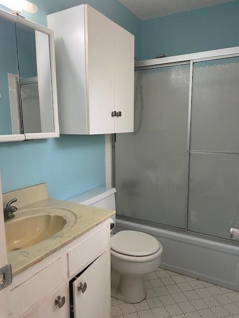 bathroom with combined bath / shower with glass door, toilet, vanity, and a textured ceiling