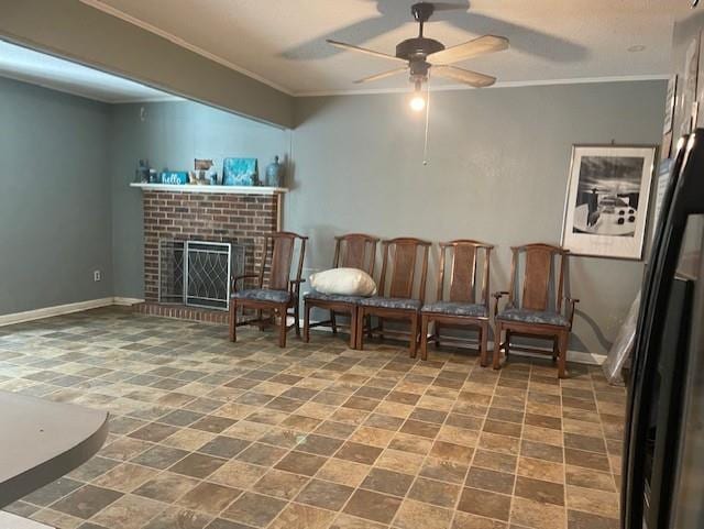 sitting room with a brick fireplace, ornamental molding, stone finish floor, baseboards, and a ceiling fan