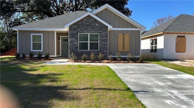 view of front of house with stone siding, board and batten siding, a front yard, and a shingled roof