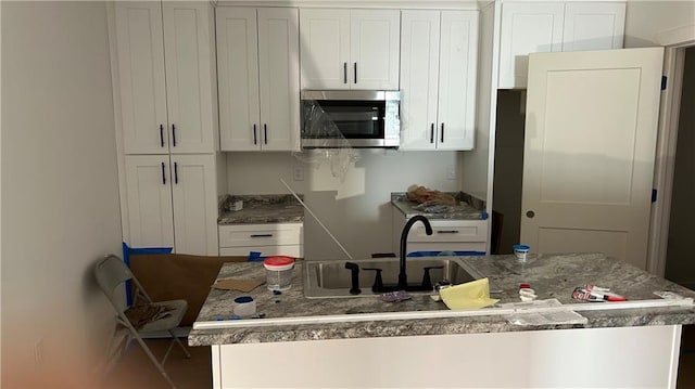 kitchen with stainless steel microwave, white cabinets, and a kitchen island with sink