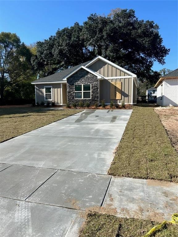 view of front of home featuring board and batten siding, a front yard, concrete driveway, and stone siding