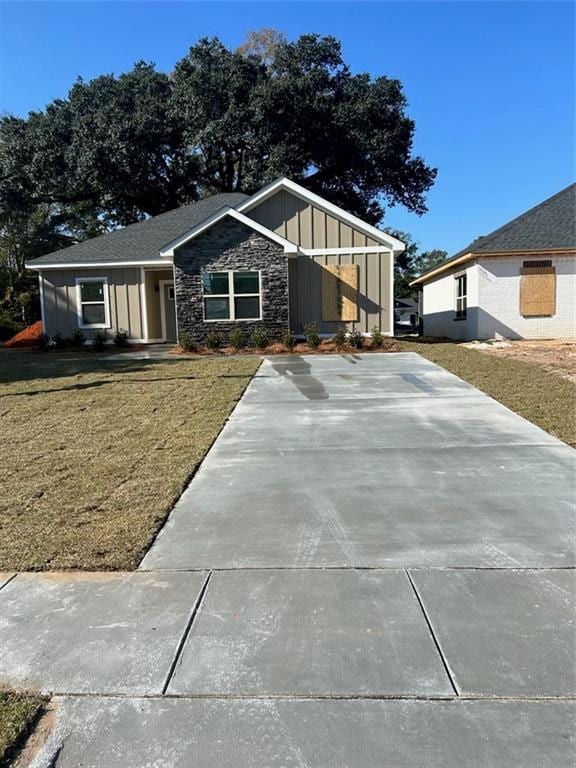 view of front of house with a front yard, driveway, board and batten siding, and stone siding