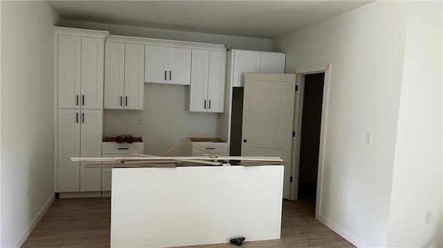 kitchen with white cabinetry, wood finished floors, baseboards, and a kitchen island