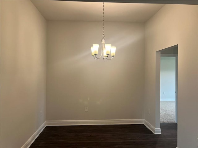 empty room with a notable chandelier, dark wood-type flooring, and baseboards