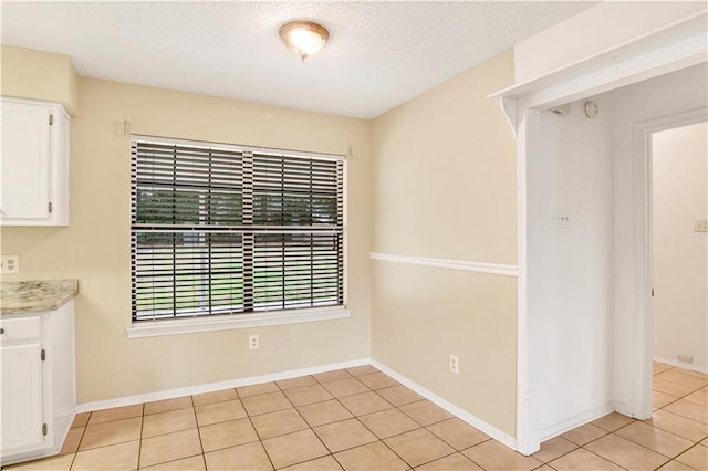 unfurnished dining area with baseboards, a textured ceiling, and light tile patterned flooring