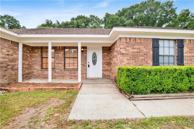 doorway to property featuring covered porch and brick siding