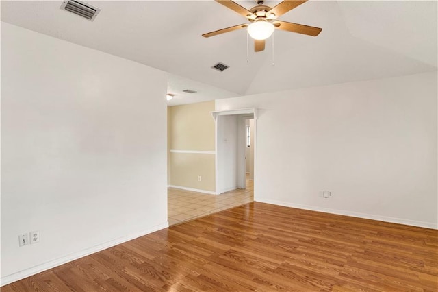 empty room featuring lofted ceiling, visible vents, light wood-style flooring, and baseboards