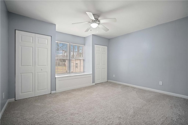 unfurnished bedroom featuring carpet floors, two closets, a ceiling fan, and baseboards