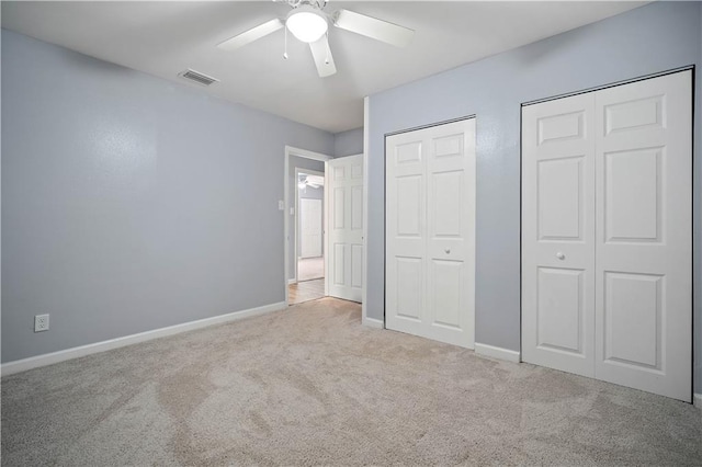 unfurnished bedroom featuring multiple closets, light colored carpet, visible vents, and baseboards