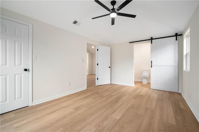 unfurnished bedroom with visible vents, a barn door, vaulted ceiling, and light wood finished floors