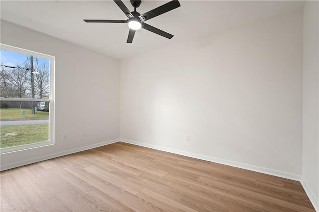 empty room featuring light wood finished floors, a ceiling fan, baseboards, and a wealth of natural light