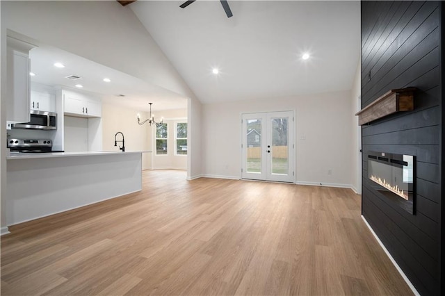 unfurnished living room featuring light wood finished floors, a large fireplace, baseboards, ceiling fan with notable chandelier, and high vaulted ceiling