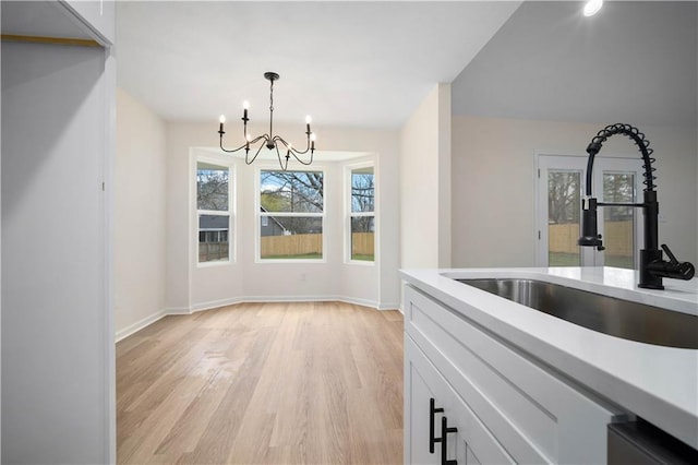 unfurnished dining area with a sink, baseboards, light wood-style floors, and an inviting chandelier