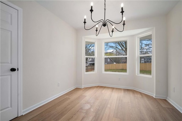 unfurnished dining area featuring baseboards, light wood-style floors, and an inviting chandelier