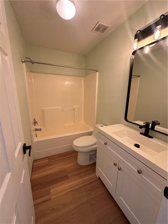 1010 Hamilton Bridges Dr E, Mobile, AL 36695 - bathroom with a textured ceiling, wood finished floors, toilet, vanity, and  shower combination