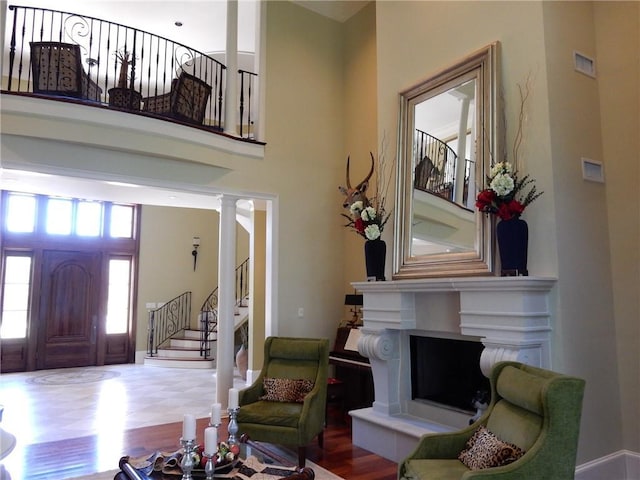 living room featuring a towering ceiling, wood-type flooring, and ornate columns