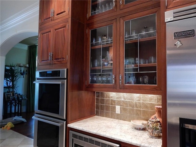 kitchen featuring light stone counters, hardwood / wood-style flooring, stainless steel appliances, backsplash, and ornamental molding