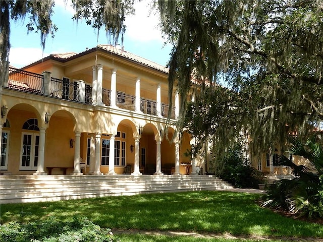 rear view of property featuring a balcony, french doors, a yard, and a patio