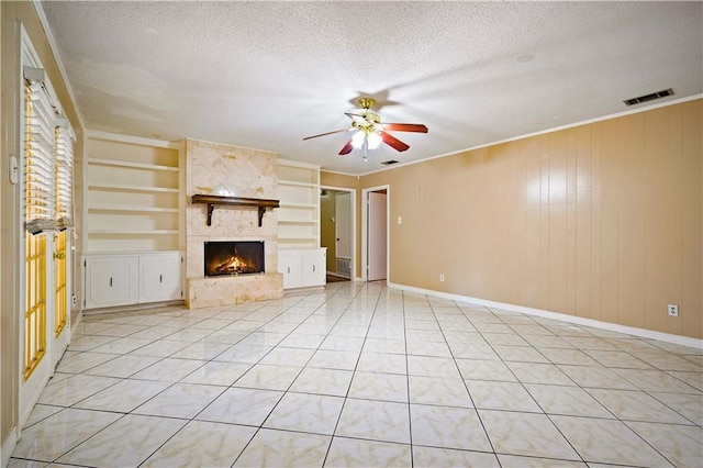 unfurnished living room featuring a fireplace, wooden walls, built in features, and a textured ceiling