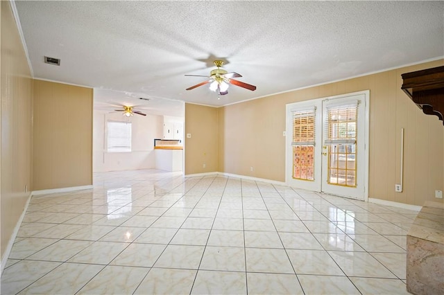 empty room featuring a textured ceiling, ceiling fan, crown molding, and light tile patterned flooring