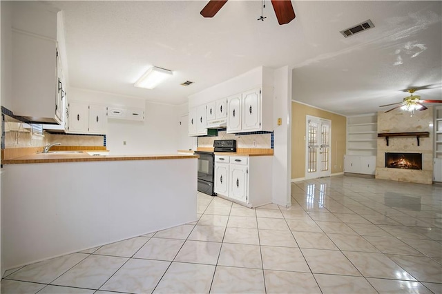 kitchen with kitchen peninsula, a large fireplace, white cabinetry, and black electric range oven