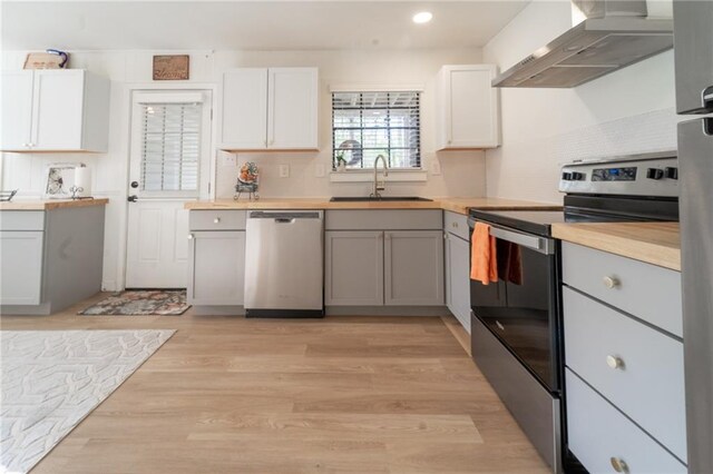 kitchen featuring a sink, wall chimney range hood, stainless steel appliances, light wood finished floors, and decorative backsplash
