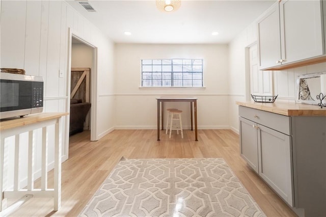 interior space with stainless steel microwave, visible vents, baseboards, light wood-type flooring, and gray cabinets