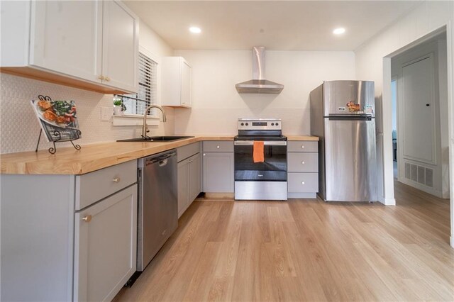 kitchen featuring gray cabinets, appliances with stainless steel finishes, light wood-style floors, wall chimney exhaust hood, and a sink