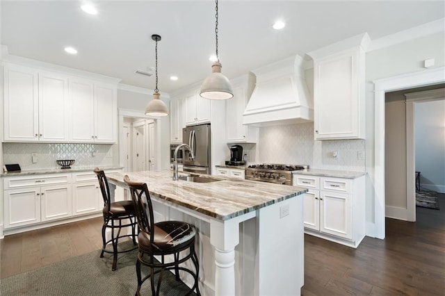 kitchen featuring custom exhaust hood, a kitchen island with sink, hanging light fixtures, light stone counters, and white cabinetry