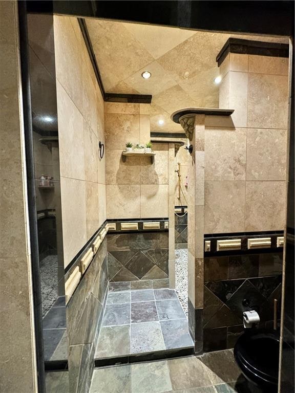 bathroom featuring toilet, a tile shower, and tile walls