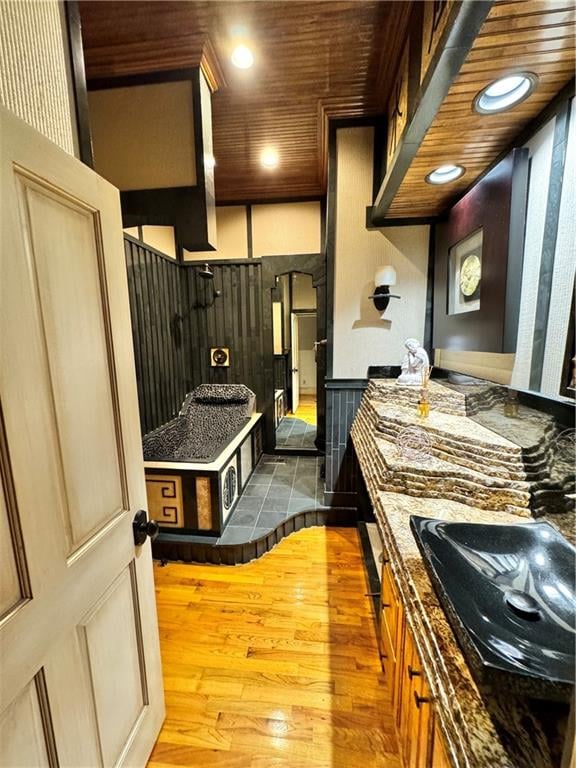 kitchen featuring light hardwood / wood-style floors, wooden ceiling, sink, and dark stone counters