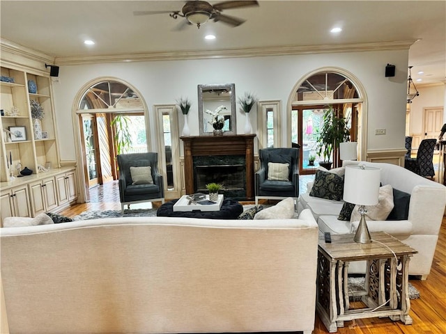 living room with a wealth of natural light, ceiling fan, ornamental molding, and light wood-type flooring